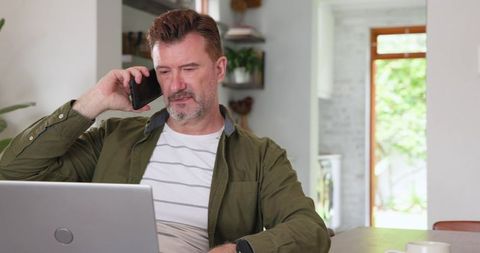 Middle-Aged Man Multitasking with Smartphone and Laptop in Cozy Home Interior