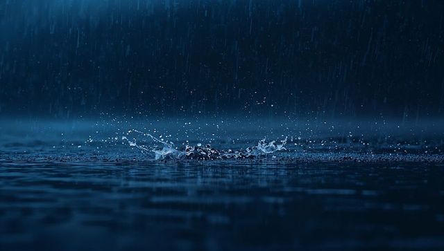 Nighttime rain splash creating crown droplets and ripples with deep blue reflections