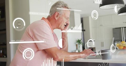 Senior man using smartphone while typing on laptop with hud data overlays in home kitchen
