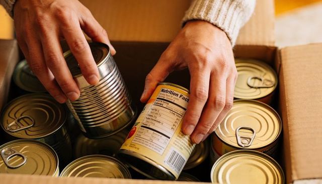 Hands packing canned goods in cardboard box close-up for pantry donation and storage