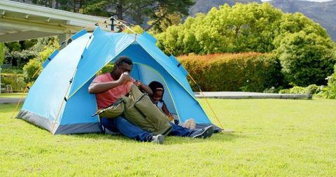 Father and Daughter Unpacking Backpack by Blue Tent on Green Lawn