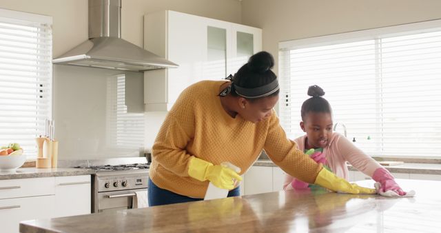 Mother and daughter cleaning kitchen counter together. They are wearing gloves while using sprays and cloths, engaging in a bonding activity. Great for family, household chores, teamwork, and parenting concepts. Suitable for use in articles, blogs, or advertisements about family life, home cleaning products, or teamwork.