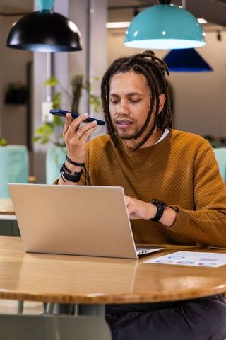 African american man recording voice message while working on laptop in coworking space