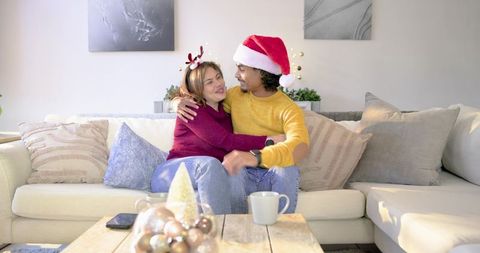 Couple cuddling on couch wearing Santa hat and reindeer antlers celebrating cozy holiday