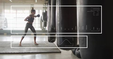 Female boxer punching heavy bag in backlit industrial gym training for strength and focus