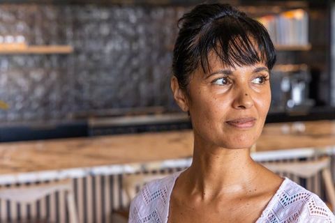 Mature african woman gazing thoughtfully while leaning on cafe counter, wearing lace top
