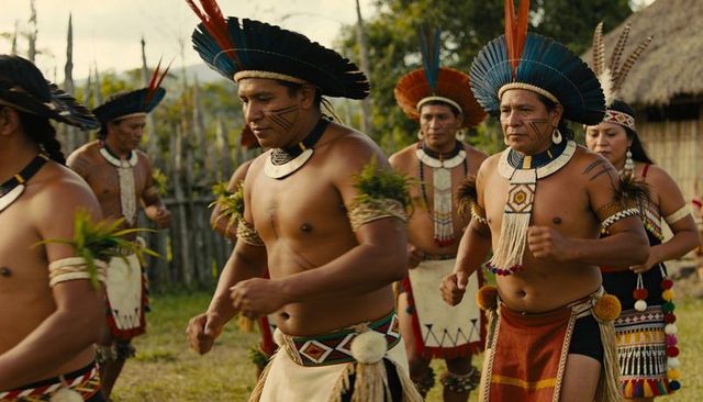 Indigenous men parading in feather headdresses and beaded regalia during ritual procession