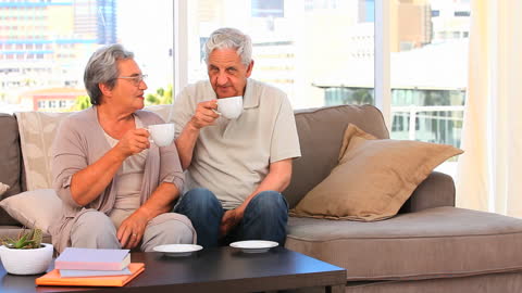 Happy Retirees Enjoying Coffee Relaxing on Couch at Home