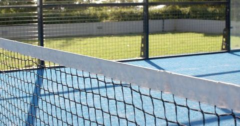 Tennis net running diagonally across blue synthetic court casting sharp sunlit shadows