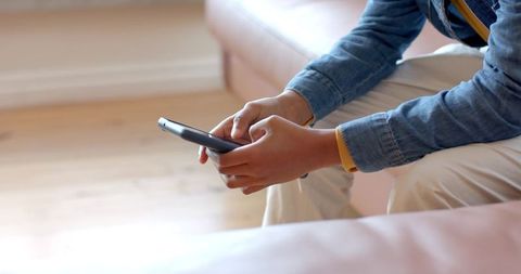 African american child sitting on sofa holding smartphone wearing denim jacket backpack