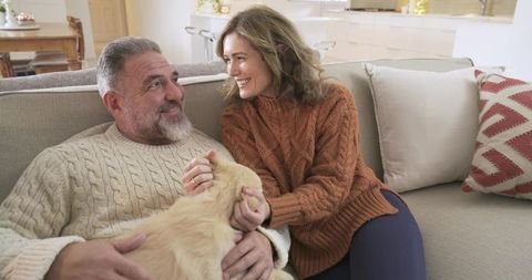 Happy couple relaxing on couch with cream-colored cat in cozy living room