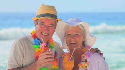 Smiling Senior Couple Enjoying Beach Vacation With Drinks