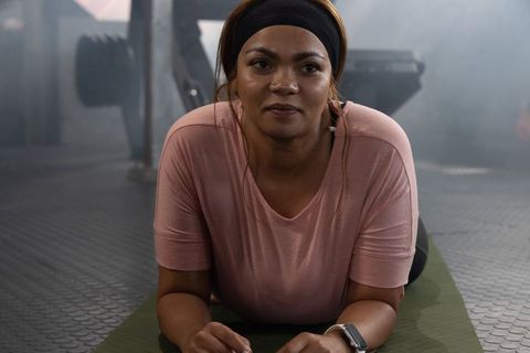 African american woman holding forearm plank on mat, wearing smartwatch and earbuds