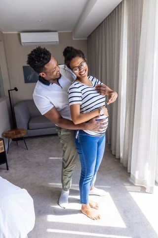 African american couple embracing and cradling pregnant belly by sunlit window