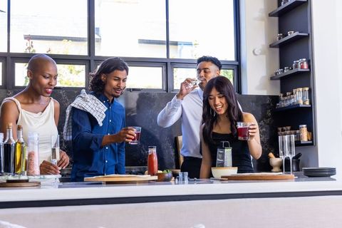 Diverse friends gathering at modern kitchen island toasting with red drinks and laughing