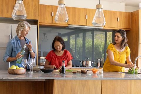 Multigenerational friends cooking in modern kitchen pouring wine chopping rinsing greens