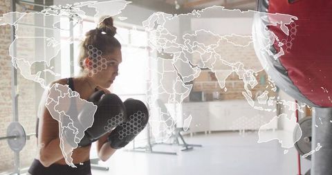 Determined woman boxing in loft gym throwing punches at heavy bag with world map overlay