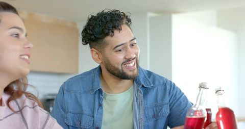 Friends sharing drinks at kitchen counter man holding capped bottle and smiling home