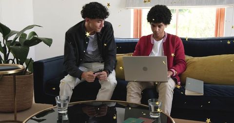 Two young professionals collaborating on laptop and smartphone on modern living room sofa