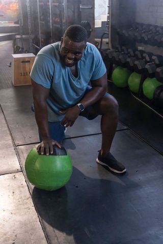 African american athlete kneeling pressing hand on green medicine ball gym workout