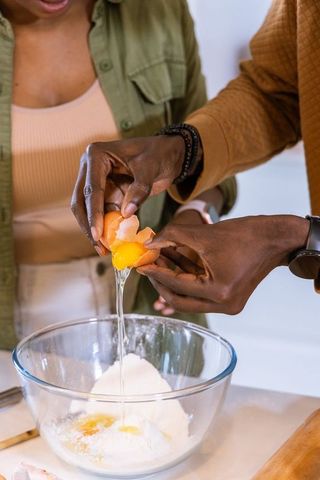 African american couple cracking eggs together preparing batter in home kitchen