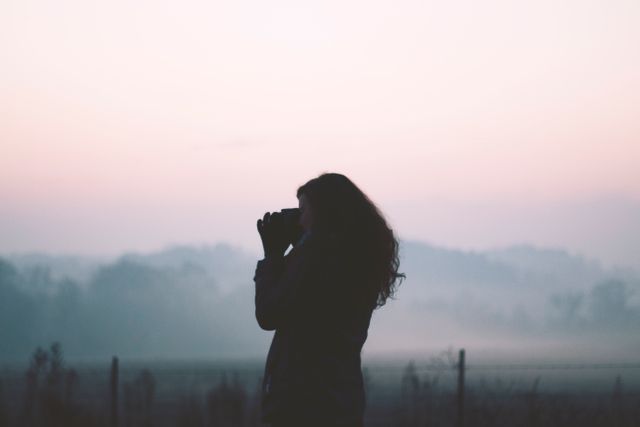 Silhouette of a woman using binoculars for birdwatching in a misty sunrise. Captures the serene ambiance and morning mist, making it perfect for emphasizing tranquility in nature, promoting outdoor activities, or showcasing birdwatching hobbies.