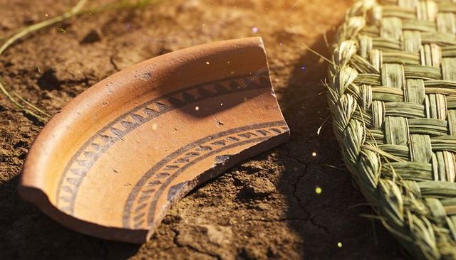 Resting terracotta shard with geometric bands on cracked soil beside woven mat