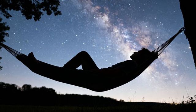 Male silhouette relaxing in hammock under milky way night sky with vivid starfield