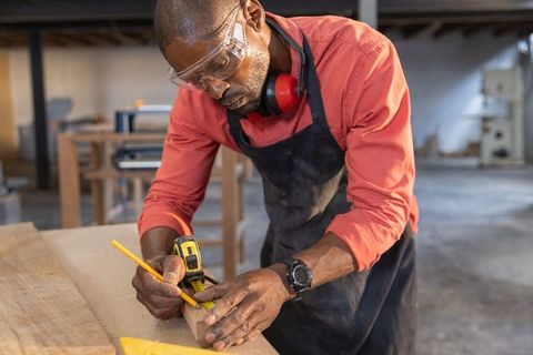 Skilled african american woodworker wearing goggles measuring and marking wood block