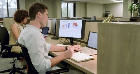 Coworkers analyzing data on screens in open office environment