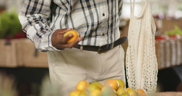 Middle-aged man shopping for fresh oranges at a farmer's market, showcasing sustainable lifestyle with a reusable produce bag. Ideal for illustrating healthy eating, sustainable living, and natural food sourcing. Perfect for content related to local markets, eco-friendly shopping habits, and organic produce.