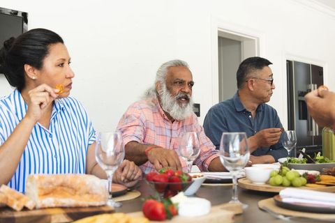 Multigenerational family sharing meal at rustic kitchen table with bread cheese and fruit