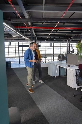 Middle-aged colleagues walking and discussing with tablet in industrial mezzanine office