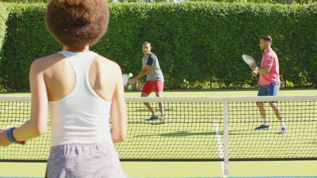 This image highlights a group of diverse friends engaging in a game of tennis under a clear sky. The players display energetic enthusiasm and camaraderie, symbolizing active lifestyles and social enjoyment. Ideal for promotional materials focusing on healthy living, community, recreational sports, or advertisements showcasing friendship and inclusivity in outdoor activities.