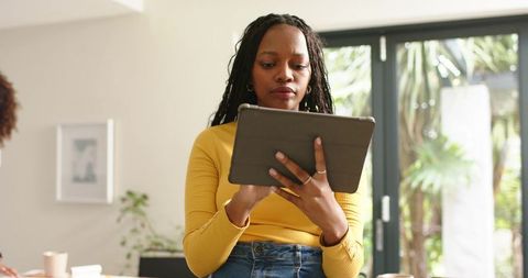 African american woman using tablet in bright home office near sliding door with coffee