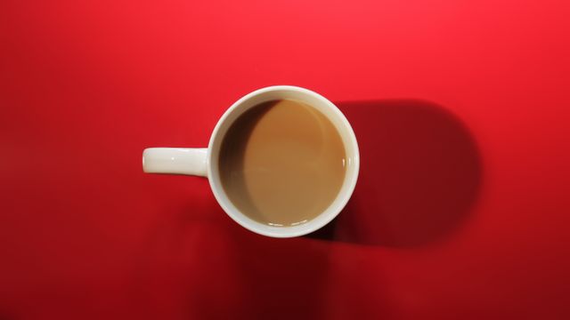 White mug filled with coffee viewed from top, placed on bright red background. Ideal for illustrating morning routines, promoting coffee-related products, or adding a splash of color to advertisements. The bold contrast between the mug and background makes it visually appealing for web and graphic designs.