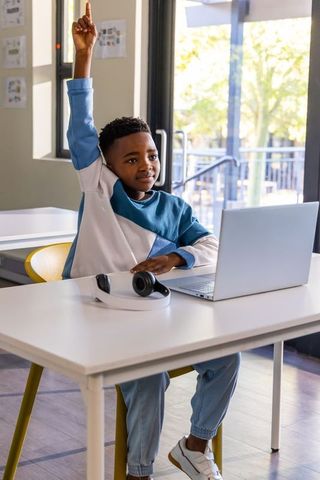 African american student raising hand at laptop in bright modern classroom