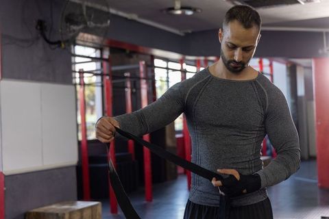 Mid-adult indian man wrapping hands for boxing training in commercial gym, fitness focus