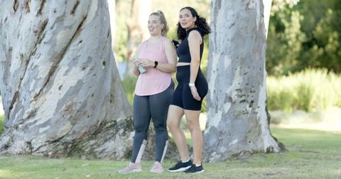 Diverse Friends in Activewear Relaxing by Trees at Park