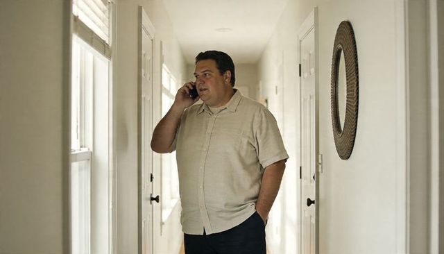 Man standing in bright hallway talking on smartphone, casual short-sleeve shirt