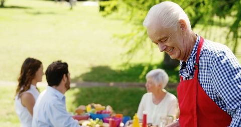 Senior Man Hosting Outdoor Picnic with Friends and Family in Park