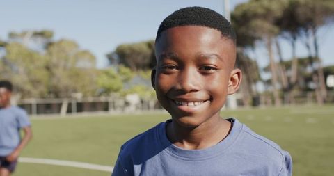 Smiling african boy standing on sunlit soccer field wearing blue athletic shirt