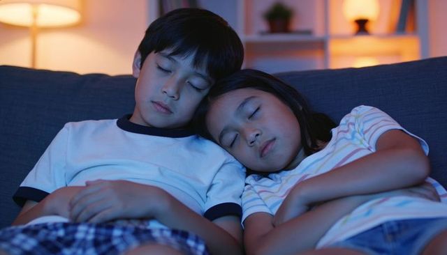 Sleeping siblings cuddling on sofa at night cozy living room warm lamp light