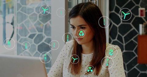 Focused woman working on laptop with sustainable tech icons overlay in modern coworking space