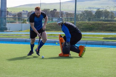 Intensity on field hockey pitch with competitive duo facing goalkeeper