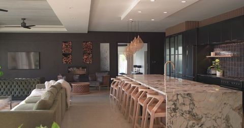 Marble waterfall kitchen island with brass faucet and wooden bar stools in open-plan luxury living i