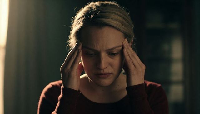 Woman holding temples in dim light expressing stress, headache, fatigue, emotional strain