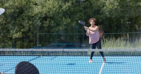 African american woman playing pickleball on blue outdoor court with paddle and net