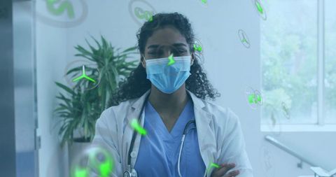 Woman physician wearing mask and scrubs visualizing green microbe safety icons in clinic