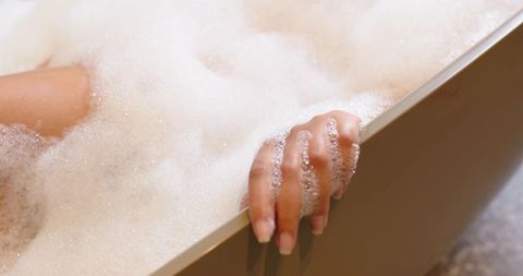 Closeup african american hand resting on freestanding tub rim with foam and soap bubbles